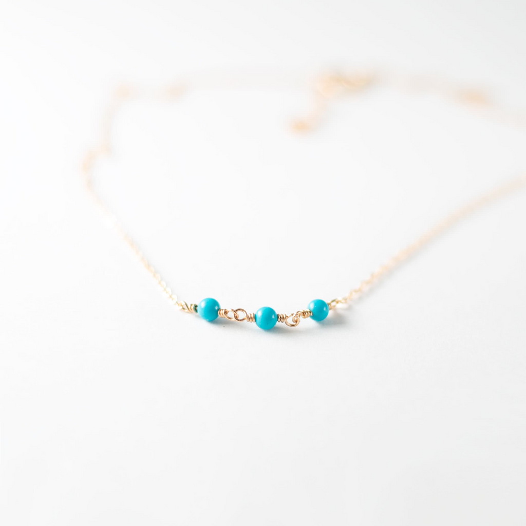 a gold necklace with turquoise beads on a white background