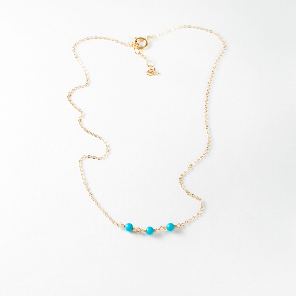 a gold chain with a turquoise beaded necklace