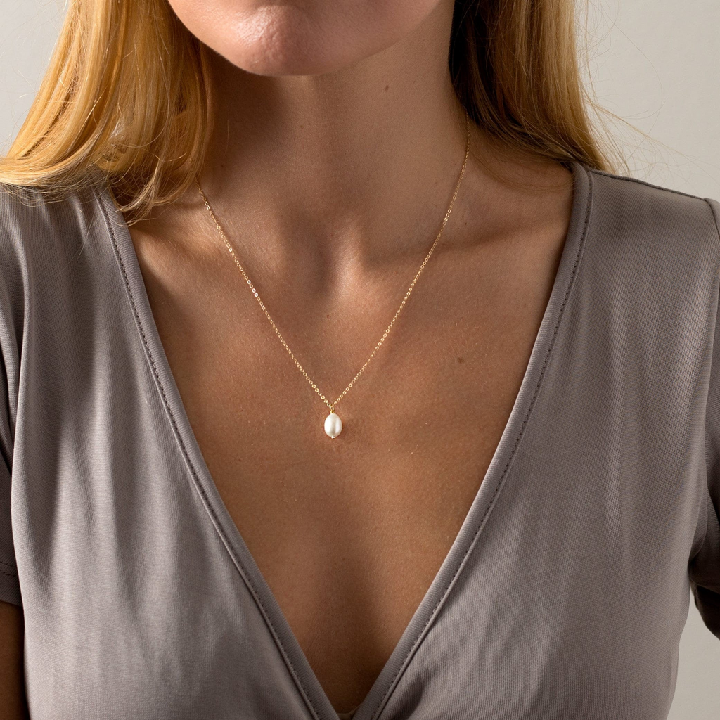 a woman wearing a necklace with a pearl