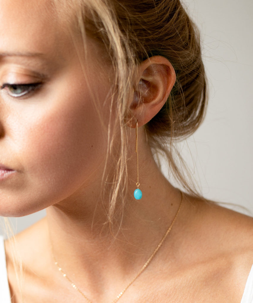 a woman wearing a necklace with a turquoise bead