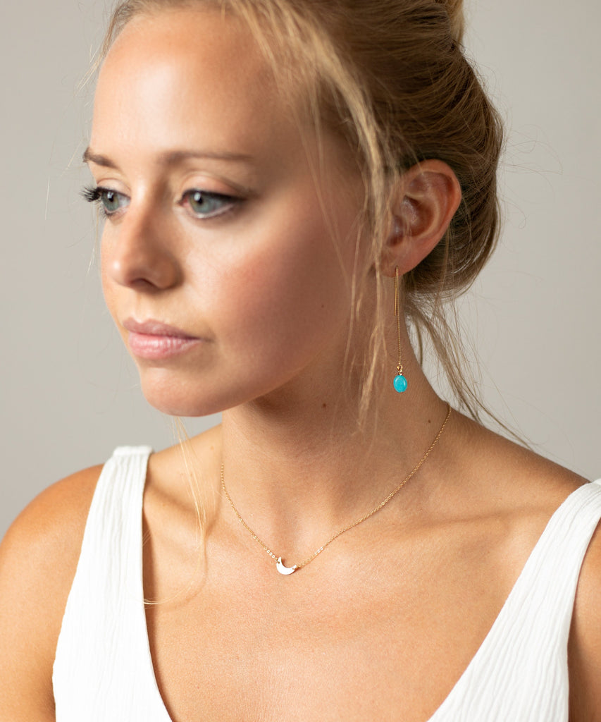 a woman wearing a white top and a blue necklace