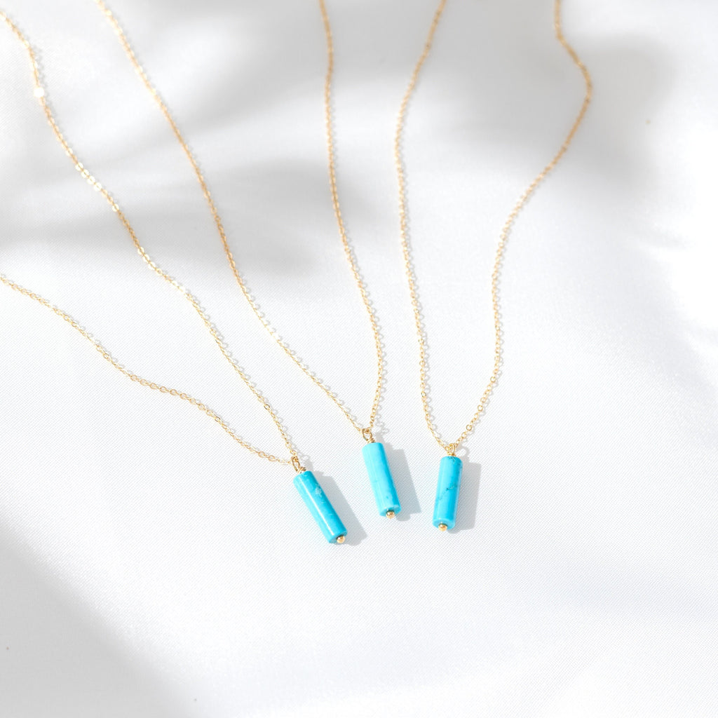 three necklaces on a white surface with a gold chain