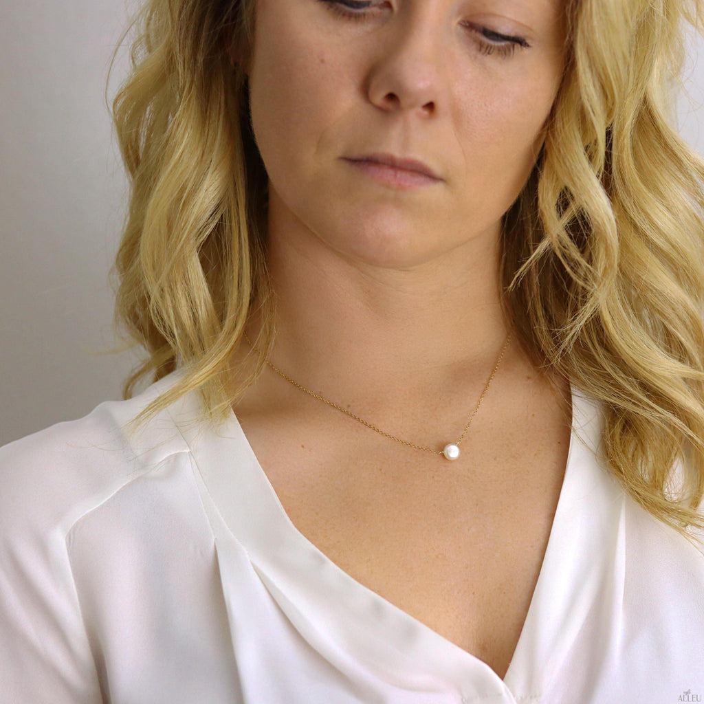 a woman wearing a necklace with a pearl on it