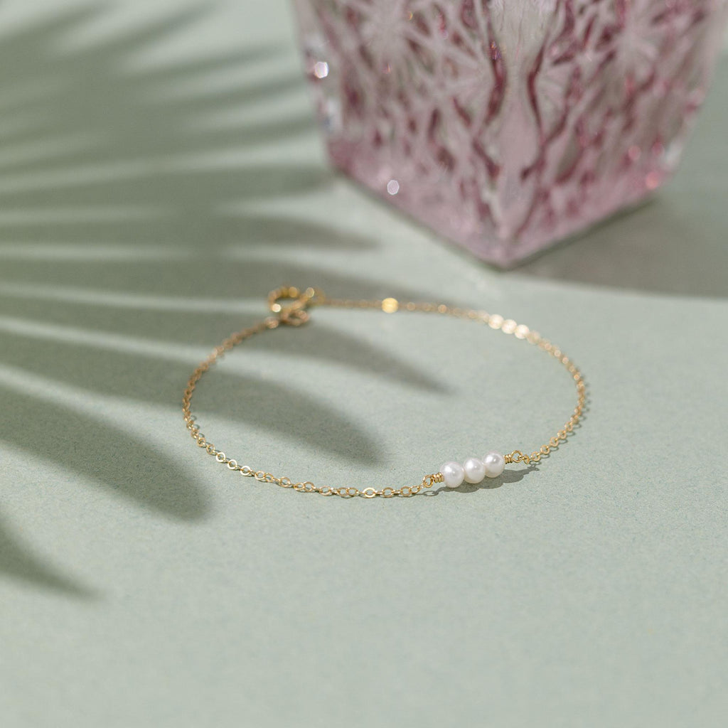 a gold bracelet with pearls sits on a table next to a pink vase