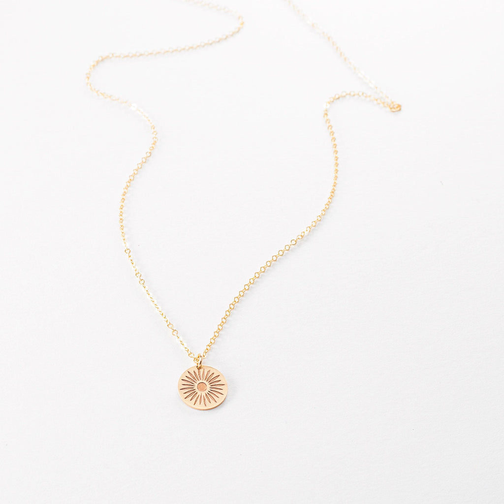 a gold necklace with a sun charm on a white background