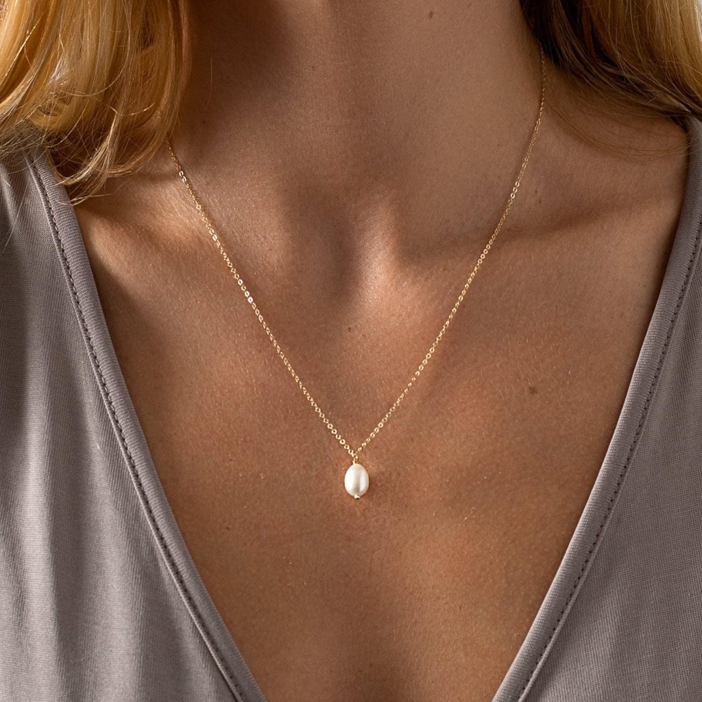 a woman wearing a necklace with a pearl